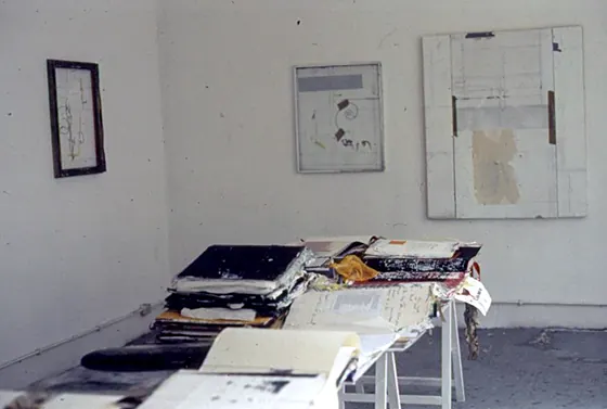 A white wall with framed works above a table of open books.