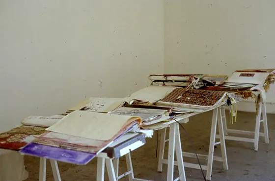 Handmade books laid out along trestle tables beside a plain wall.