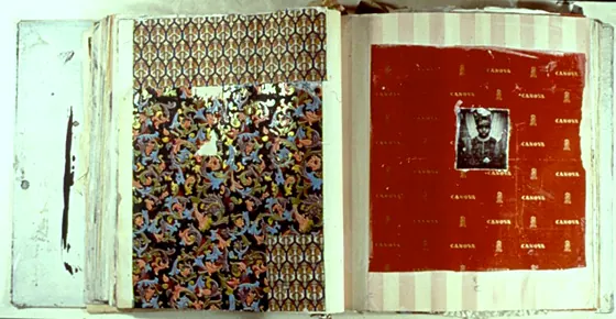 An open book with a red page holding a small portrait photograph, beside patterned fabric.