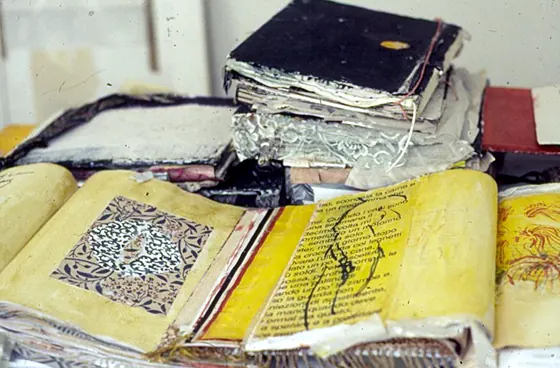 An open yellow book with a black and white ornament and handwriting, with other books stacked above.