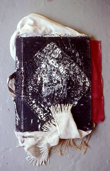 A black book cover printed with a white pattern and tied with cream fringe.